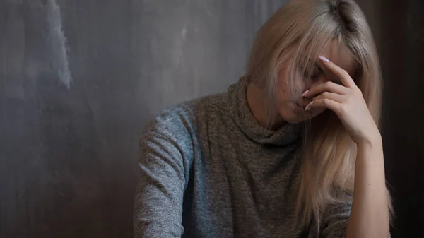Грустная молодая женщина сидит у стены. Молодая блондинка. Депрессия и проблемы — стоковое фото