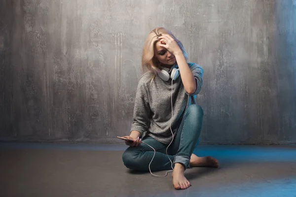 Fiatal és vonzó nő smartphone és nagy fejhallgató, ült a földön. Zene a mobil app. — Stock Fotó