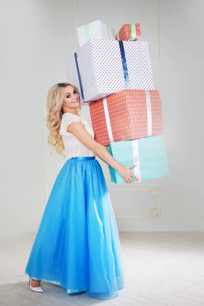 Grappige en mooie blonde met een bos van grote geschenkdozen. Charmante jongedame in een bochtige blauwe rok. — Stockfoto