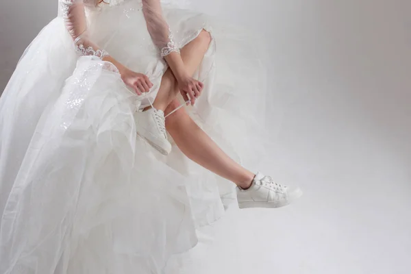 Het meisje in prachtige trouwjurk en witte sneakers, benen close-up. Runaway bride — Stockfoto