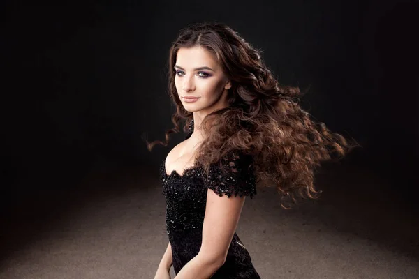 Prachtige brunette meisje in elegante zwarte jurk. Mooi lang krullend haar. — Stockfoto