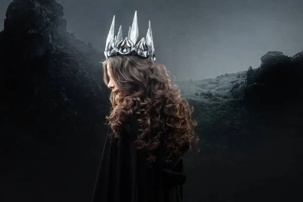Retrato de uma princesa gótica. Mulher morena jovem bonita em coroa de metal e capa preta . — Fotografia de Stock