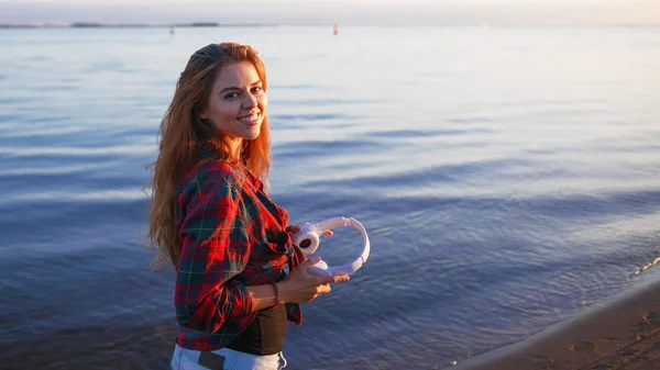 Glücklich attraktive rothaarige Mädchen genießt Lieblingsmusik auf Spaziergängen. schöne junge Frau im Hemd benutzt Kopfhörer — Stockfoto