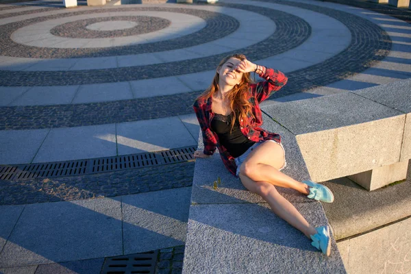 Linda jovem ruiva sentada à beira-mar, desfrutando da natureza e do bom tempo. A menina de camisa xadrez vermelho — Fotografia de Stock