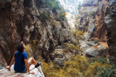 Doğayla bütünleşmiş bir gezgin, bir kayanın üzerinde genç bir adam oturuyor.