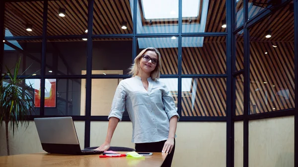 Uma jovem mulher de negócios no escritório. Trabalho no escritório, uma menina profissional fica perto da mesa com um laptop , — Fotografia de Stock