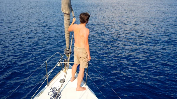 Hombre en pantalones cortos se encuentra en la cubierta cerca de la vela, vela y yate, concepto . — Foto de Stock