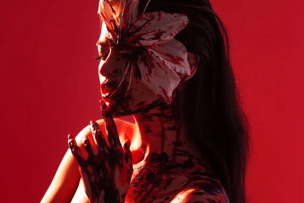 Blood Lily, děsivý a sexy Halloweenský vzhled. Krásná mladá brunetka dívka na červeném pozadí. — Stock fotografie