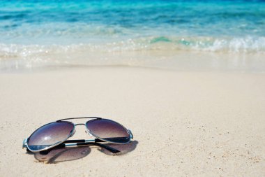 Mavi dalga arka planında beyaz kumda güneş gözlüğü. Sıcak denizde bir tatil.
