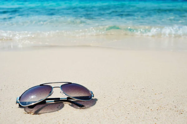 Occhiali da sole su sabbia bianca su sfondo blu onda. Vacanza al mare caldo — Foto Stock