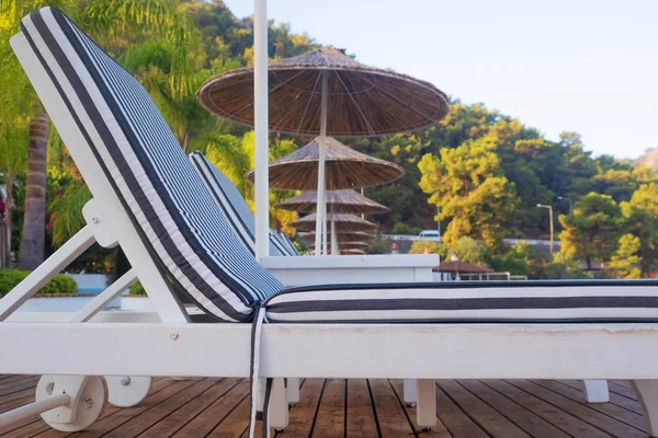 Lettini e ombrelloni di paglia in spiaggia. Bella passeggiata con sedie a sdraio in fila — Foto Stock