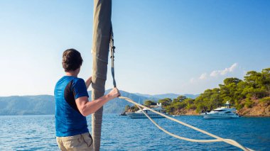 Mavi tişörtlü adam güvertede yelkenin yanında duruyor, yelkencilik ve yat, konsept..