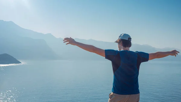 Young man stands on top with his arms outstretched, against the sea and the horizon. — Stock Photo, Image