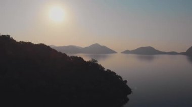 Gün batımı ya da gün doğumu, sakin deniz ve dağlar, ufukta güneş,