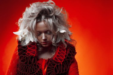Kırmızının tonları. Kırmızı bir kıyafet içinde garip çekici kadın, kırmızı bir arka plan üzerinde, saçında zambak çiçekleri ile.