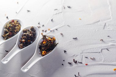 Beyaz desenli arka planda çay yapraklarının farklı çeşitleri kaşıkları ölçer. Çay demlemeye.