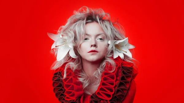 Tonos de rojo. Mujer atractiva, en un vestido rojo, posando sobre un fondo rojo, con flores de lirio blanco en el pelo . — Foto de Stock