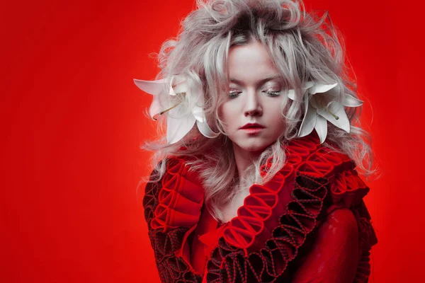 Tonos de rojo. Mujer atractiva, en un vestido rojo, posando sobre un fondo rojo, con flores de lirio blanco en el pelo . —  Fotos de Stock