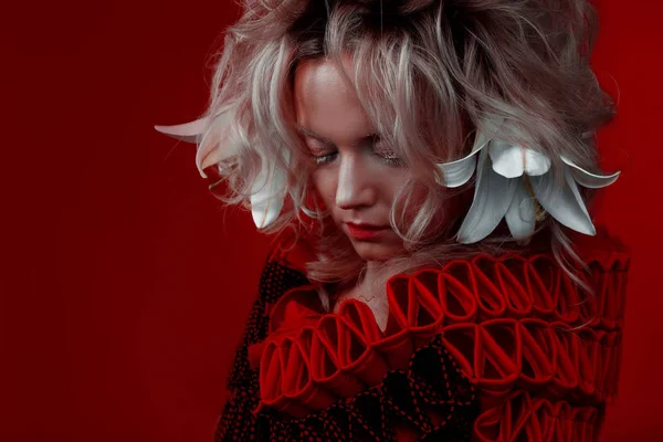 Tonos de rojo. Extraña mujer atractiva en un traje rojo, sobre un fondo rojo, con flores de lirio en el pelo . —  Fotos de Stock