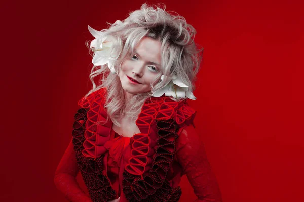 Shades of red. Strange attractive woman in a red outfit, on a red background, with lily flowers in her hair. — Stock Photo, Image