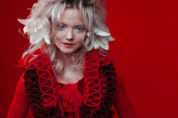 Αποχρώσεις του κόκκινου. Παράξενη ελκυστική γυναίκα με κόκκινη στολή, σε κόκκινο φόντο, με λουλούδια από τη Λίλι στα μαλλιά της. — Φωτογραφία Αρχείου