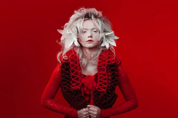 Tonos de rojo. Mujer atractiva, en un vestido rojo, posando sobre un fondo rojo, con flores de lirio blanco en el pelo . — Foto de Stock