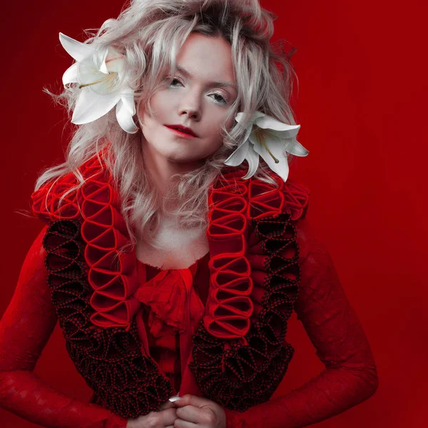 Rottöne. seltsame attraktive Frau in rotem Outfit, auf rotem Hintergrund, mit Lilienblüten im Haar. — Stockfoto