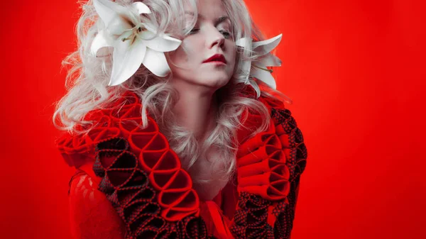 Árnyalatú piros. Furcsa, vonzó nő egy piros ruhában, egy piros háttér, a liliom virágok a haját. — Stock Fotó