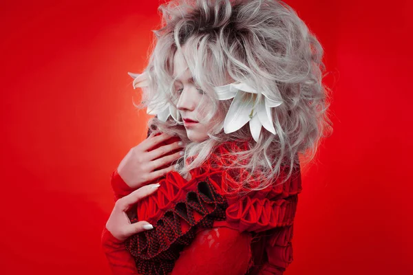 Tonos de rojo. Mujer atractiva, en un vestido rojo, posando sobre un fondo rojo, con flores de lirio blanco en el pelo . — Foto de Stock