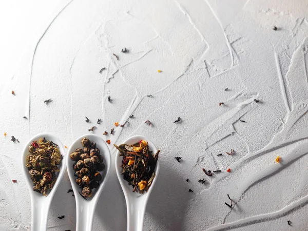 Diferentes variedades de hojas de té en cucharas blancas que miden sobre un fondo de textura blanca. Para preparar té — Foto de Stock