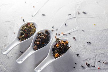 Beyaz desenli arka planda çay yapraklarının farklı çeşitleri kaşıkları ölçer. Çay demlemeye.