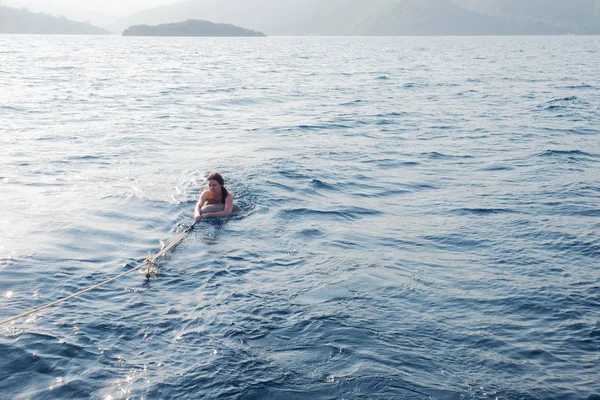 一位年轻女子从船上拖出水面，紧紧抓住绳子，在船后游泳 — 图库照片