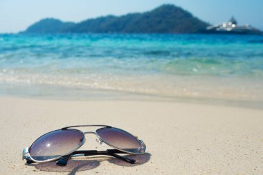 Mavi dalga arka planında beyaz kumda güneş gözlüğü. Sıcak denizde bir tatil.