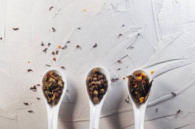 Beyaz desenli arka planda çay yapraklarının farklı çeşitleri kaşıkları ölçer. Çay demlemeye.