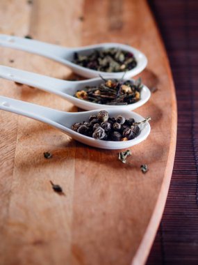 Tahta bir masada beyaz kaşıklarla çay yapraklarının farklı çeşitleri. Çay demlemeye.