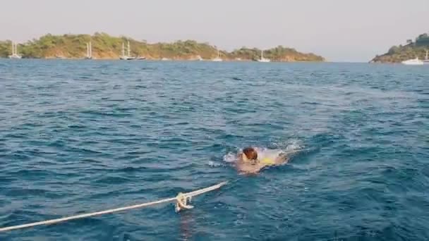 Pulled out of the water on Board a boat, a young woman swims behind a boat holding on to a rope — Stock Video