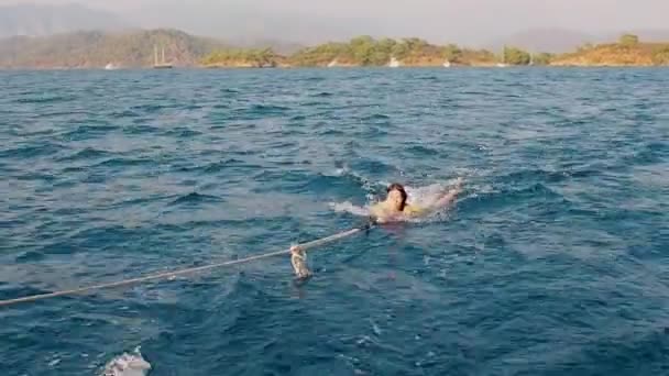 Dras upp ur vattnet ombord på en båt, en ung kvinna simmar bakom en båt som håller i ett rep — Stockvideo
