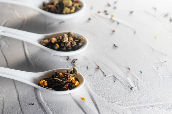 Diferentes variedades de folhas de chá em colheres de medição brancas em um fundo branco texturizado. Para preparar o chá — Fotografia de Stock
