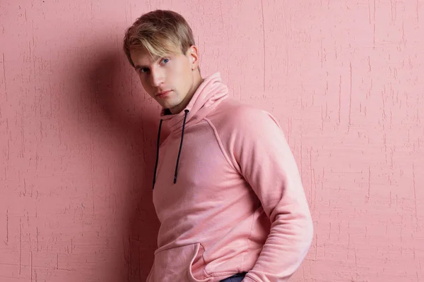 Young man in a pink hoodie on a pink background, happy and smiling — Stock Photo, Image