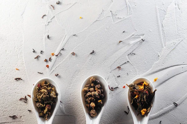 Diferentes variedades de folhas de chá em colheres de medição brancas em um fundo branco texturizado. Para preparar o chá — Fotografia de Stock