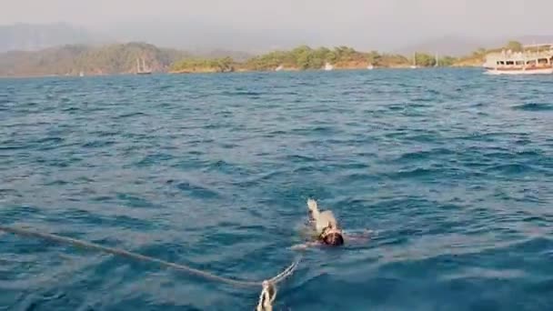 Sacada del agua a bordo de un barco, una joven mujer nada detrás de un barco sujetándose a una cuerda — Vídeos de Stock