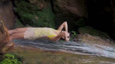 Genç bir kadın bir şelalenin suyunda yüzünü yıkıyor. Dağlarda küçük bir şelale, doğa