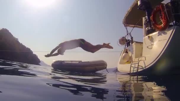 Chicos divertidos se sumergen en el mar desde el lado de un yate de vela. Acción de tiro desde el agua , — Vídeo de stock