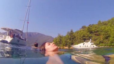 Mayolu genç bir kadın yelkenli bir yatın yanında denizde yüzüyor..