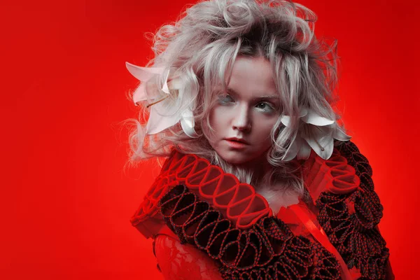 Tonos de rojo. Extraña mujer atractiva en un traje rojo, sobre un fondo rojo, con flores de lirio en el pelo . — Foto de Stock