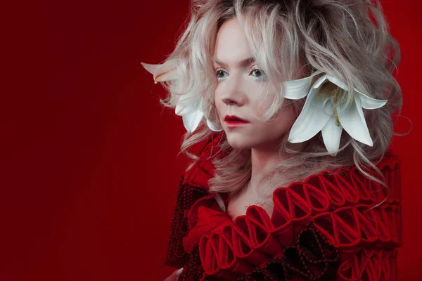 Tonalità di rosso. Donna attraente, in abito rosso, in posa su uno sfondo rosso, con fiori di giglio bianco tra i capelli . — Foto Stock