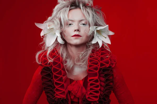 Αποχρώσεις του κόκκινου. Ελκυστική γυναίκα, σε ένα κόκκινο φόρεμα, ποζάρει σε κόκκινο φόντο, με λευκά λουλούδια κρίνο στα μαλλιά της. — Φωτογραφία Αρχείου
