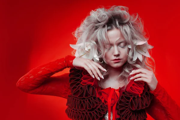 Tonos de rojo. Extraña mujer atractiva en un traje rojo, sobre un fondo rojo, con flores de lirio en el pelo . — Foto de Stock