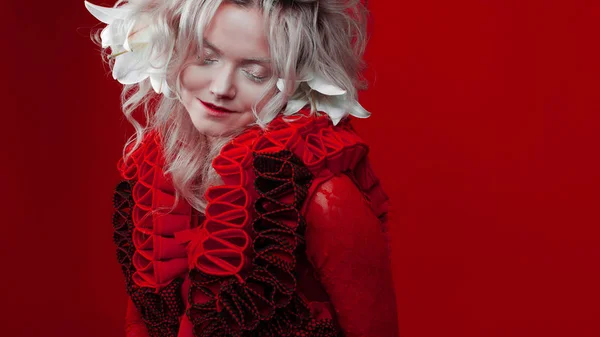 Shades of red. Strange attractive woman in a red outfit, on a red background, with lily flowers in her hair. — Stock Photo, Image