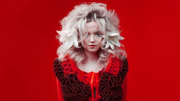 Tonos de rojo. Extraña mujer atractiva en un traje rojo, sobre un fondo rojo, con flores de lirio en el pelo . — Foto de Stock